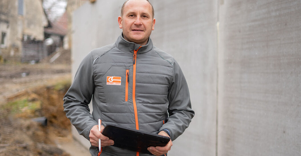 Leyrer + Graf Mitarbeiter steht mit Tablet auf einer Baustelle und blickt lächelnd in die Kamera