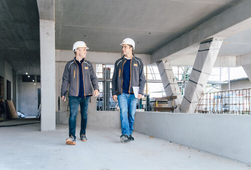 Zwei Leyrer + Graf Mitarbeiter gehen auf einer Baustelle und einer der beiden hält dabei einen Plan