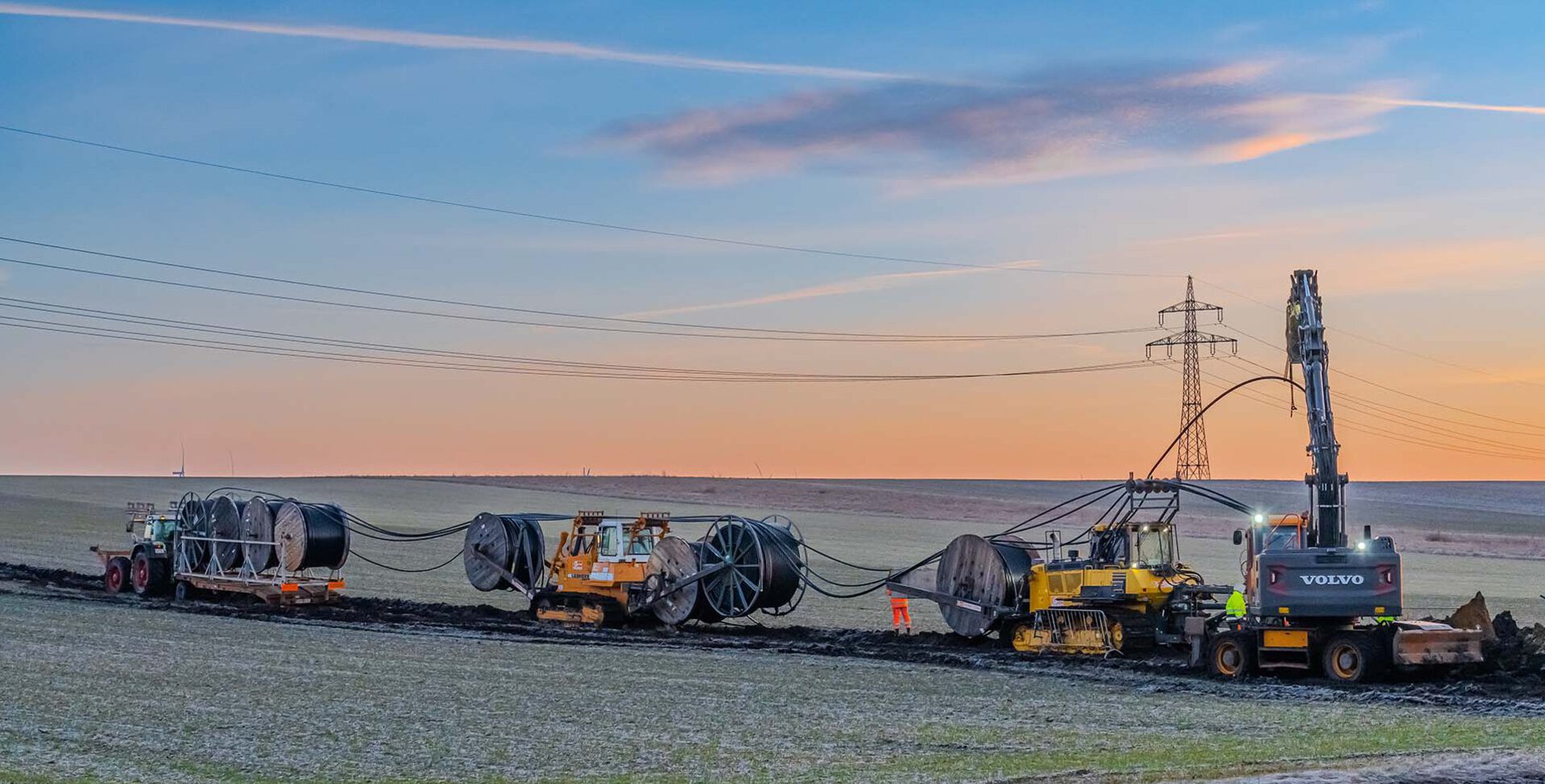 Zahlreiche Großgeräte, wie Kabelpflug beim verlegen einer Leitung im Sonnenaufgang