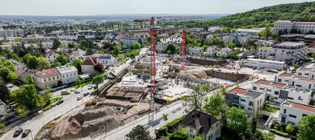 Leyrer + Graf Bauvorhaben Wohnhausanlage Grutschgasse, Mödling in der Bauphase mit rotem Kran und grüner und städtischer Umgebung 