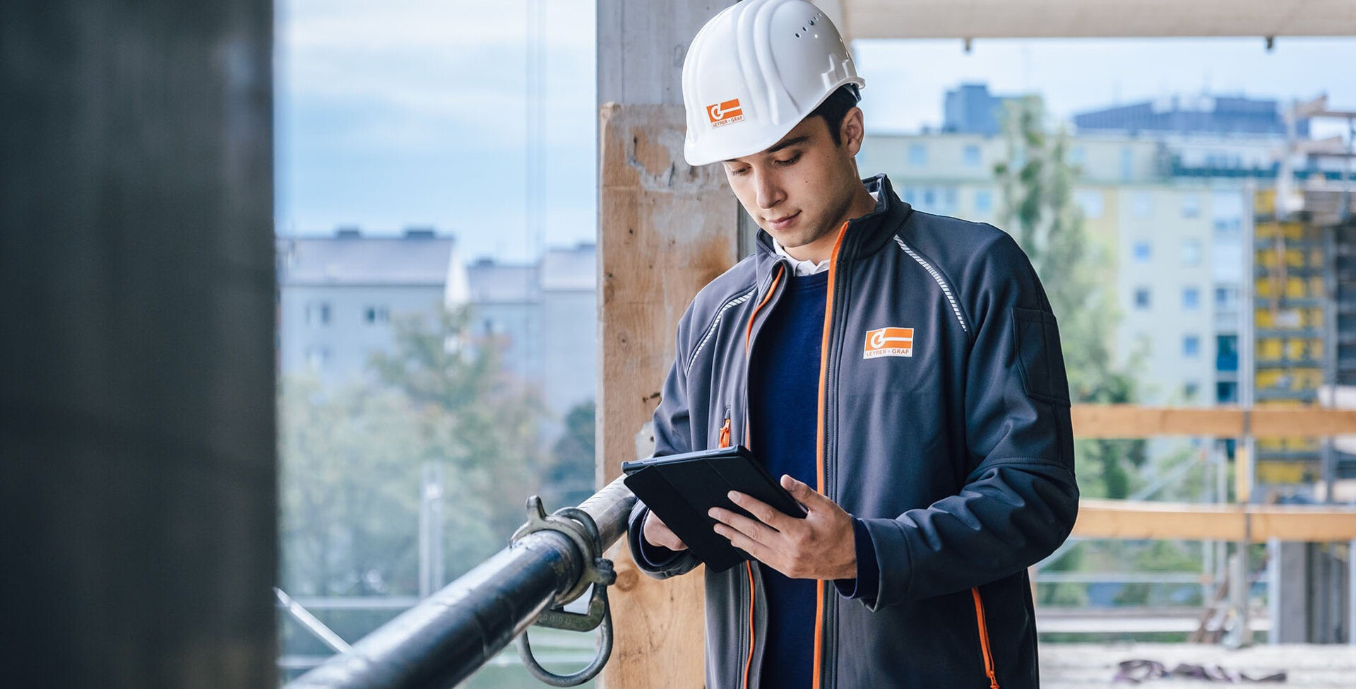 Ein Leyrer + Graf Mitarbeiter stehen auf einer Baustelle und arbeitet an seinem Tablet