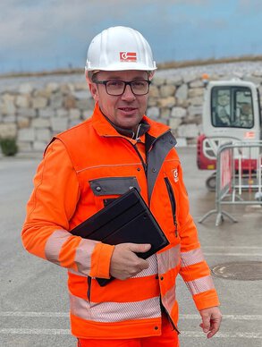 Leyrer + Graf Mitarbeiter steht vor einer Baustelle und lächelt in die Kamera