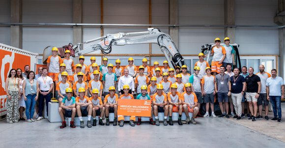 Lehrlinge der Firma Grema in Gmunden posieren vor einem Bagger in Arbeitskleidung