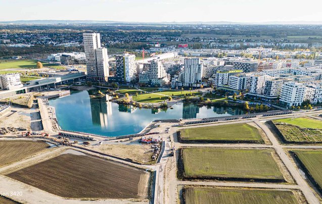 Tiefbau Bauvorhaben Leyrer + Graf - See wird auf einer Seite von Gebäuden umkreist und von der anderen Seite führen noch nicht fertiggestellt Straßen und Wege zum See und zur Stadt
