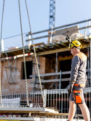 Ein Leyrer + Graf Mitarbeiter auf einer Baustelle neben ihm wird ein Betonelement mittels Kran hochgehoben